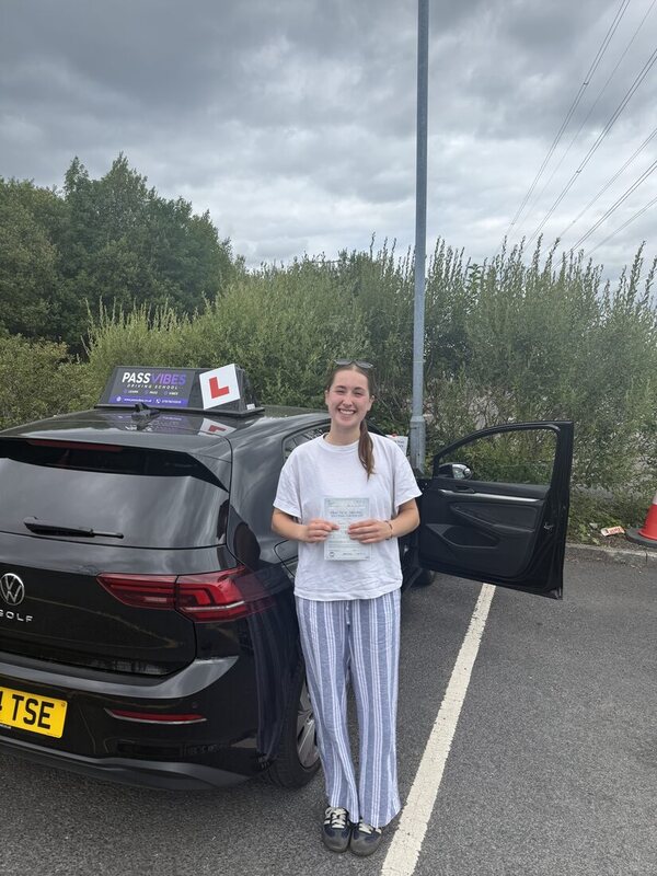 PassVibes learner holding her pass certificate beside the PassVibes driving school car after passing her driving test in Greater Manchester